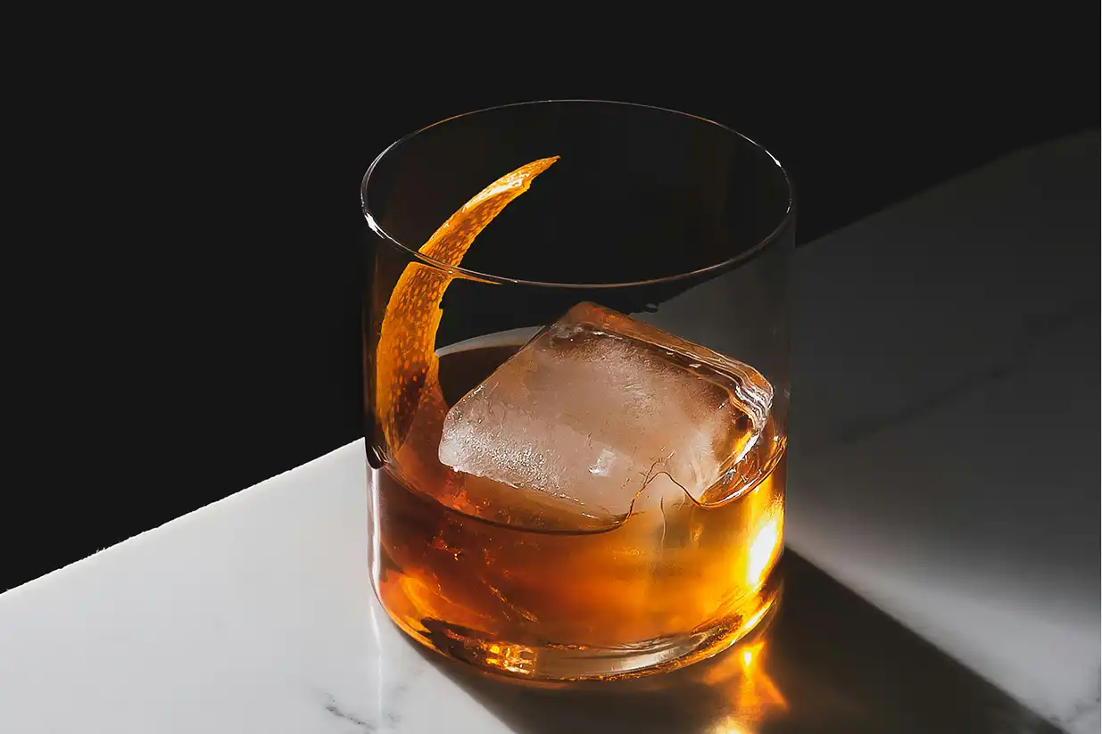 čaša viskija sa ledom na mramornoj podlozi. a glass of whisky with ice cube on marble table