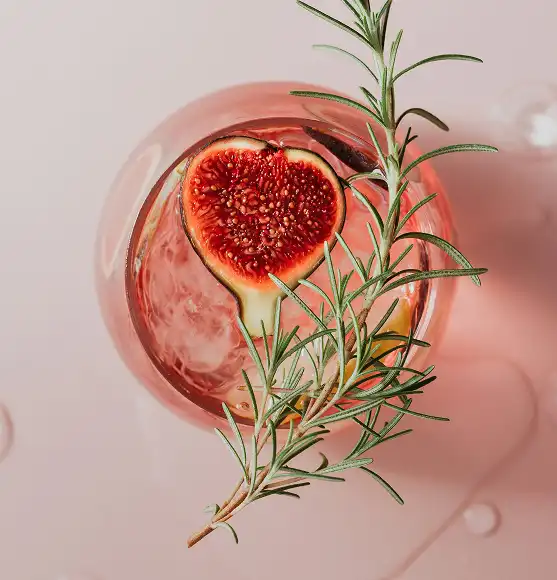 čaša gin tonika slikana sa vrha. u njoj se vidi smokva i grančica ružmarina na vrhu