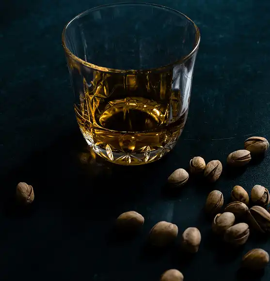 čaša viskija kraj koje su razbacani pistaciji