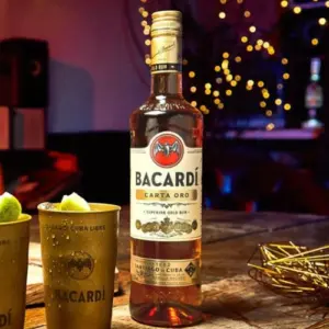 Boca Bacardi Carta Oro gold rum na stolu pokraj koktela sa limetom za dekoraciju