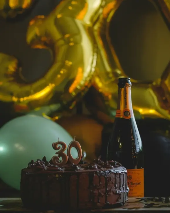 Veuve Clicquot Champagne pokraj čokoladne torte i iza zlatni baloni u obliku broja 30
