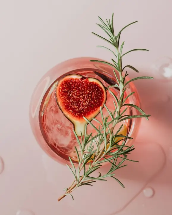 čaša gin tonika slikana sa vrha. u njoj se vidi smokva i grančica ružmarina na vrhu