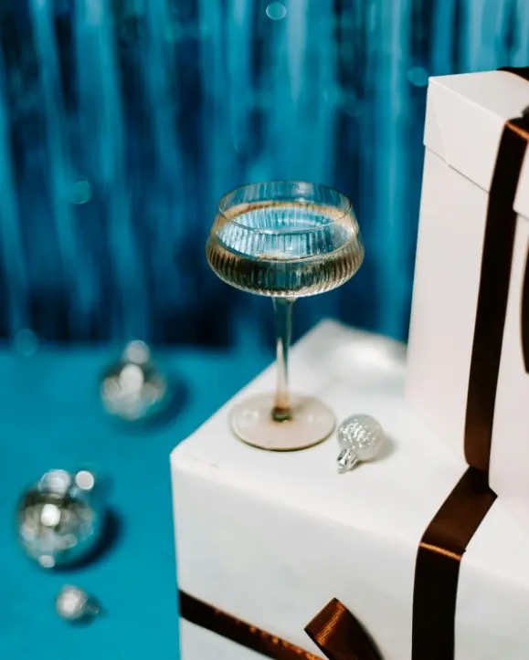 čaša pjenušca stoji na poklonu, u pozadini srebrene kuglice za bor