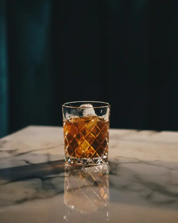 rezbarena čaša s viskijem i ledem unutra na mramornoj podlozi