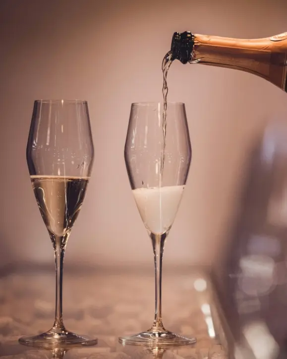 dvije čaše pjenušavog vina i vrh boce kako toči u jednu