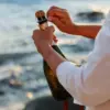 otvaranje boce pjenušca uz more. prosecco, champagne ili cava